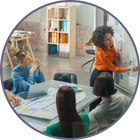 A group of colleagues gather around a table while one of them illustrates ideas on a whiteboard